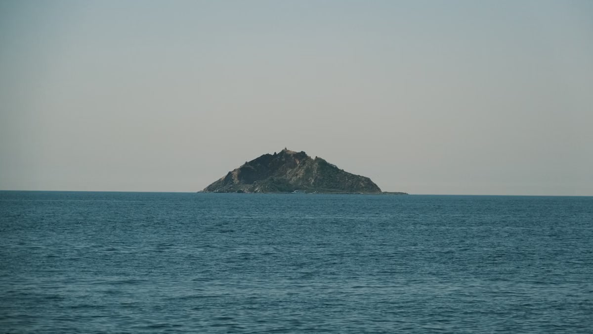 A serene view of a solitary island surrounded by calm blue ocean under a clear sky.