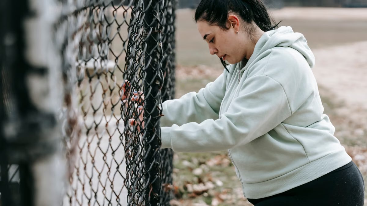 Side view of calm overweight female in sportswear standing near metal fence in park in daytime